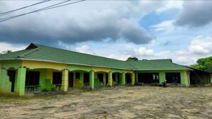 A two-story building with a green roof and yellow walls, featuring a covered outdoor area with a stone floor. - OYO 3243 3 Be Garden Hotel (Penajam)