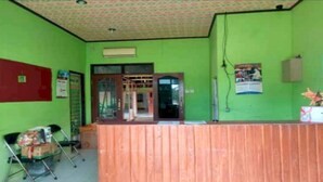 A reception area with a wooden counter, a green wall, and a patterned ceiling. - OYO 3243 3 Be Garden Hotel (Penajam)