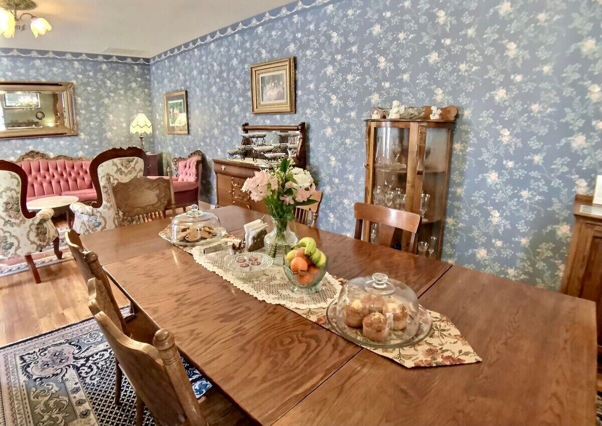 A dining room with a wooden table set for a meal, surrounded by floral wallpaper and vintage furniture.