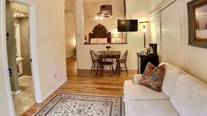 A living room with a white sofa, a dining table with chairs, a TV mounted on the wall, and a ceiling fan. - Large Suite, Iconic building! North side downtown (Eureka Springs)