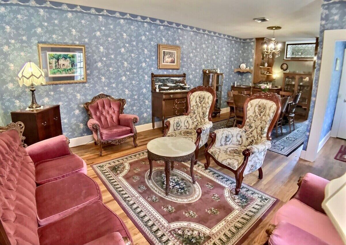 A traditional living room with a patterned wallpaper, vintage furniture, and a chandelier.