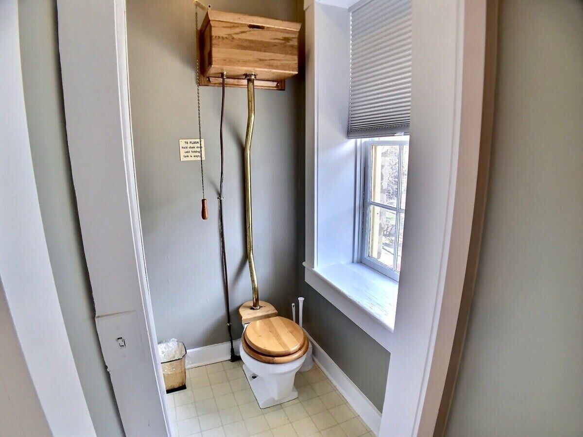 Un bagno piccolo con il water, una finestra e un armadietto in legno sopra il water.