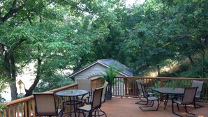 Une terrasse en bois, agréée de meubles d’extérieur, et entourée d’arbres.