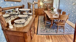 Un coin repas avec une table et des chaises en bois, entouré d’un tapis à motifs, et une cuisine au style rétro en arrière-plan.