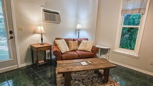 Ein Wohnzimmer mit einem braunen Ledersofa, zwei Beistelltischen mit Lampen, einem Holztisch und einem gemusterten Teppich.