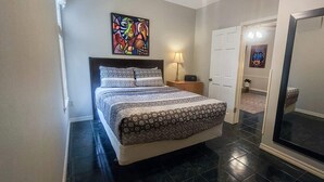 A bedroom with a bed, a nightstand, a lamp, a door, and a mirror. - The Moderne Suite Downtown Balcony, Parking (Eureka Springs)