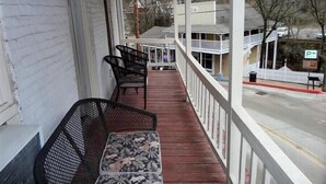 A covered porch with two black metal chairs and a bench, a white fence, and a parking sign in the background. - The Moderne Suite Downtown Balcony, Parking (Eureka Springs)