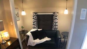 Ein gemütliches Wohnzimmer mit einer schwarzen Couch, zwei kleinen runden Tischen, einer Lampe und gemusterten Vorhängen.