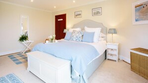 A bedroom with a bed, bedside tables, a nightstand, a mirror, a door, and a wall with framed pictures. - Beautiful 5-bed House in Port Isaac (Port Isaac)