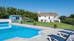A swimming pool with lounge chairs, a small blue shed, and a white house with a garden. - Beautiful 5-bed House in Port Isaac (Port Isaac)