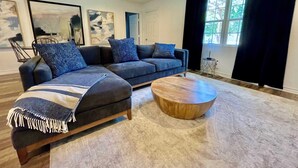 A modern living room with a sectional sofa, a round coffee table, and artwork on the walls. - Serenity Stay - 3BR 2BA - South Lubbock (Lubbock)