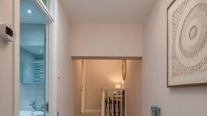 En hall med ett mattbeklätt golv, en trappa med ett träräcke, en taklampa och ett inramat konstverk på väggen.