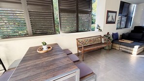 A room with a wooden table, a bench, a sofa, and a window with blinds.