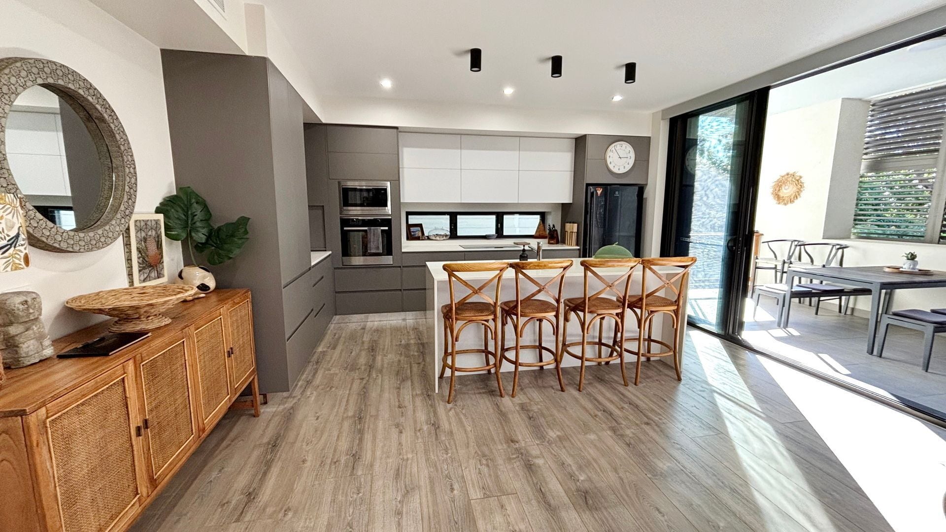 A modern kitchen with a central island, wooden bar stools, and a dining area with a large window.