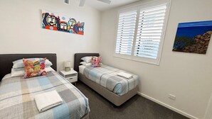 A bedroom with two beds, a nightstand, a painting, and a window with blinds. - Aurora on Gregory Apartment (South West Rocks)