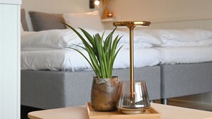 A bed with white linens, a bedside table with a plant and a glass, and a bedside lamp. - Rold Gl. Kro (Arden)