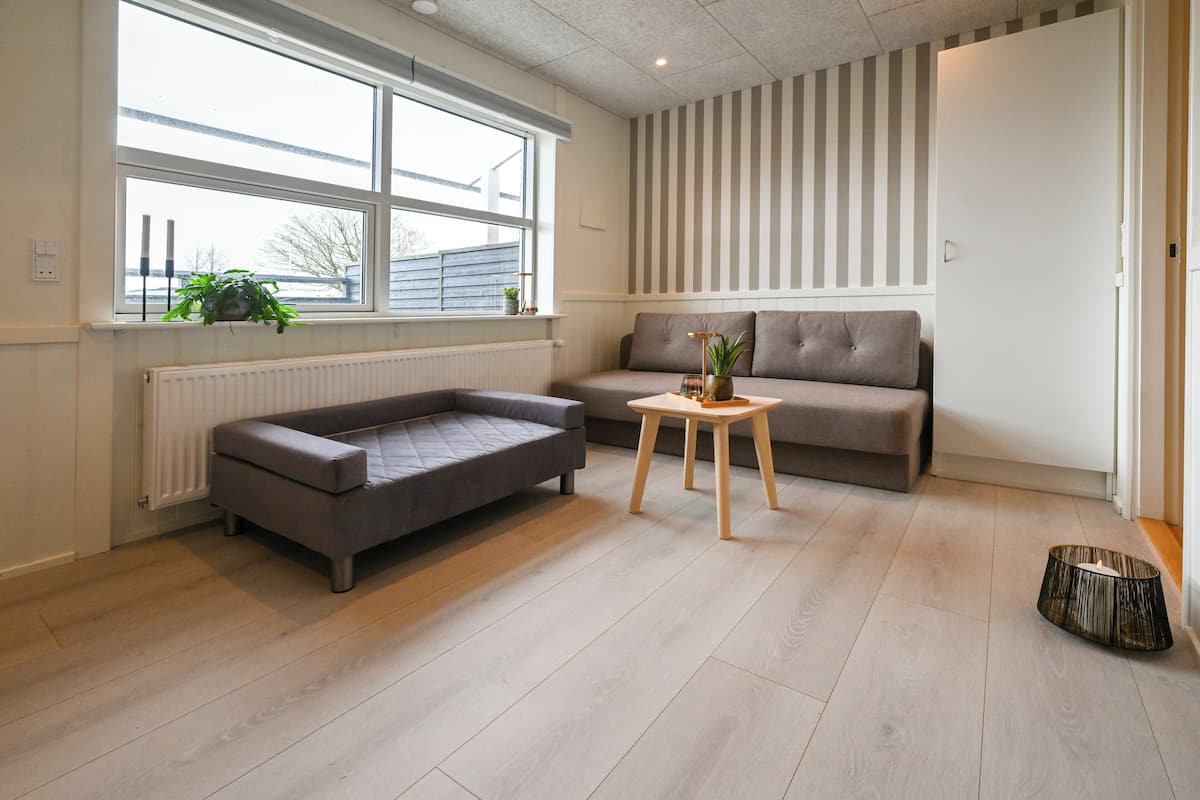 A modern living room with a grey sofa, a small wooden table with a plant, and a radiator under a window.