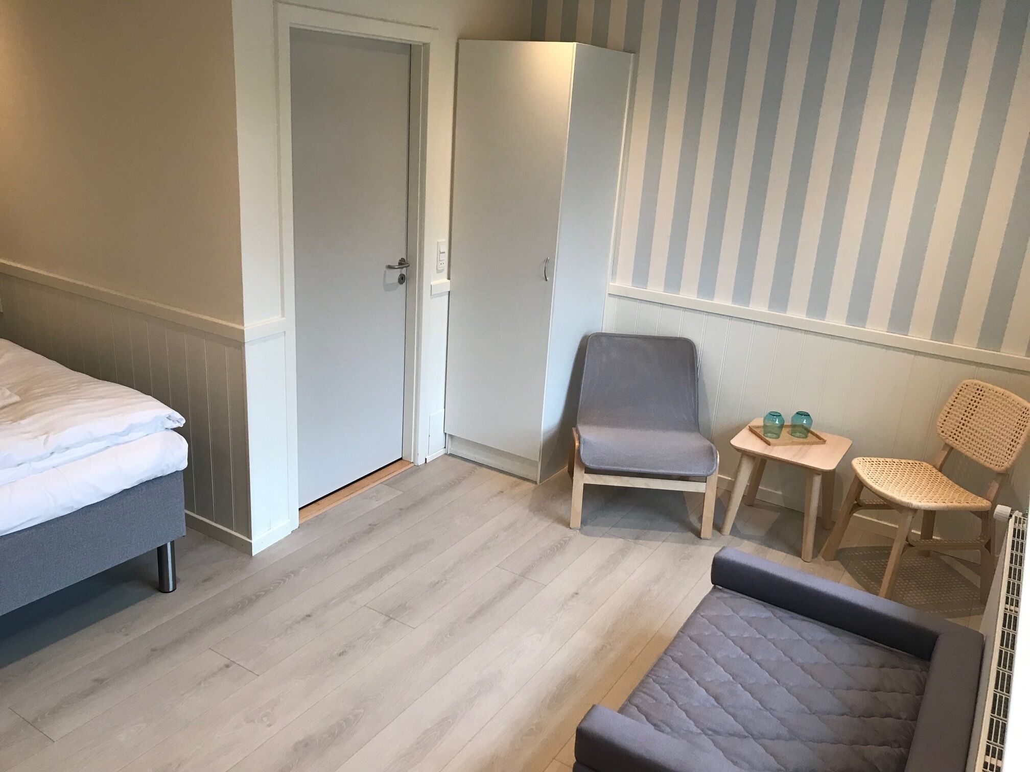 A room with a bed, a chair, a small table, and a striped wall.