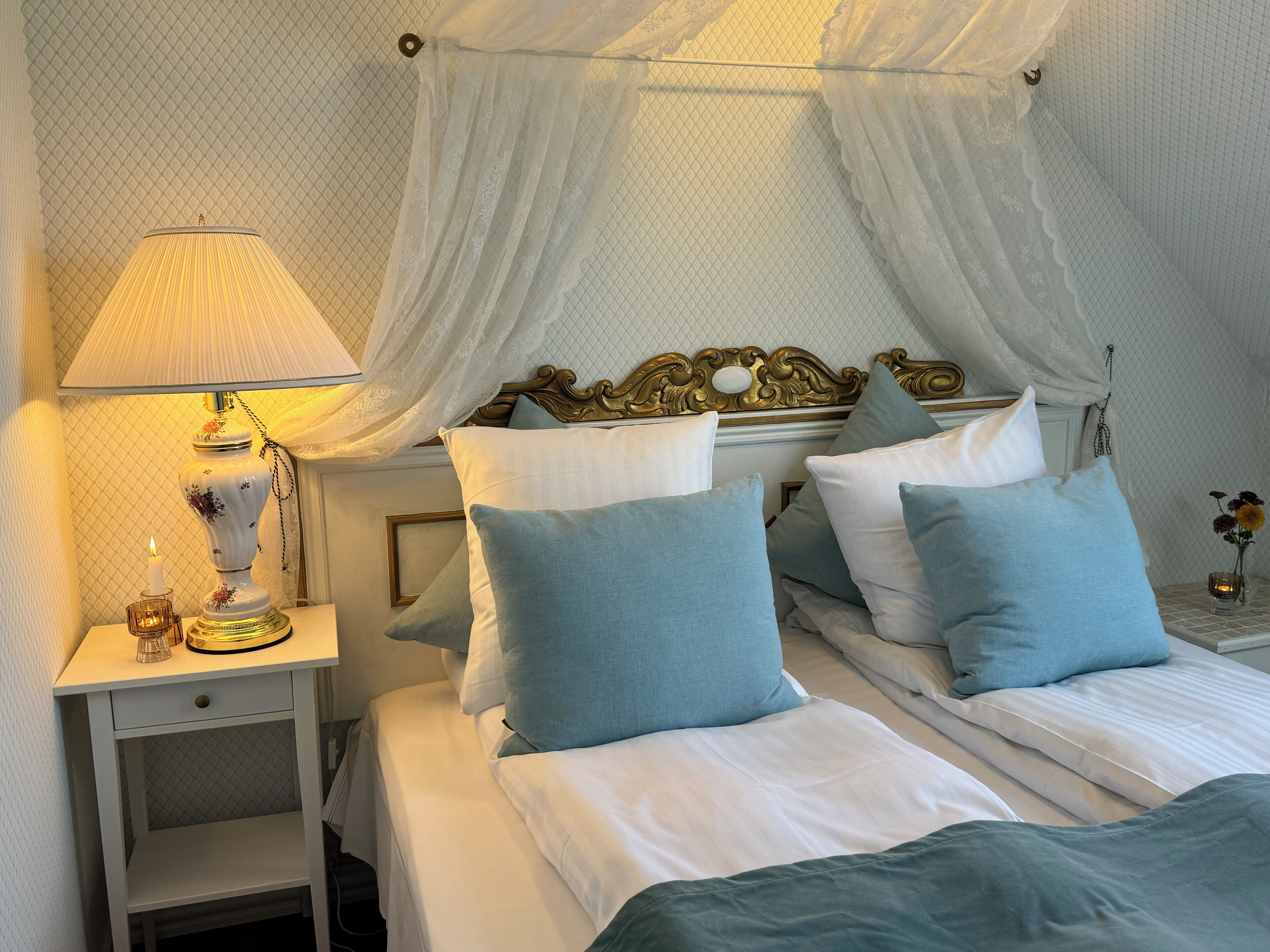 A neatly made bed with blue and white pillows, a bedside table with a lamp, and a decorative mirror above the bed.