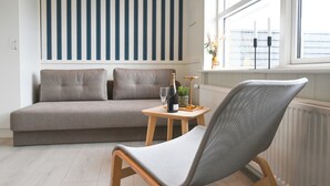 A modern living room with a grey sofa, a grey woven chair, a small wooden table with a bottle and glass, and a window with a view. - Rold Gl. Kro (Arden)