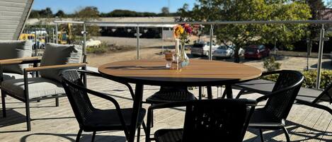 Un patio al aire libre con una mesa redonda de madera, sillas de metal negro y un florero con flores.