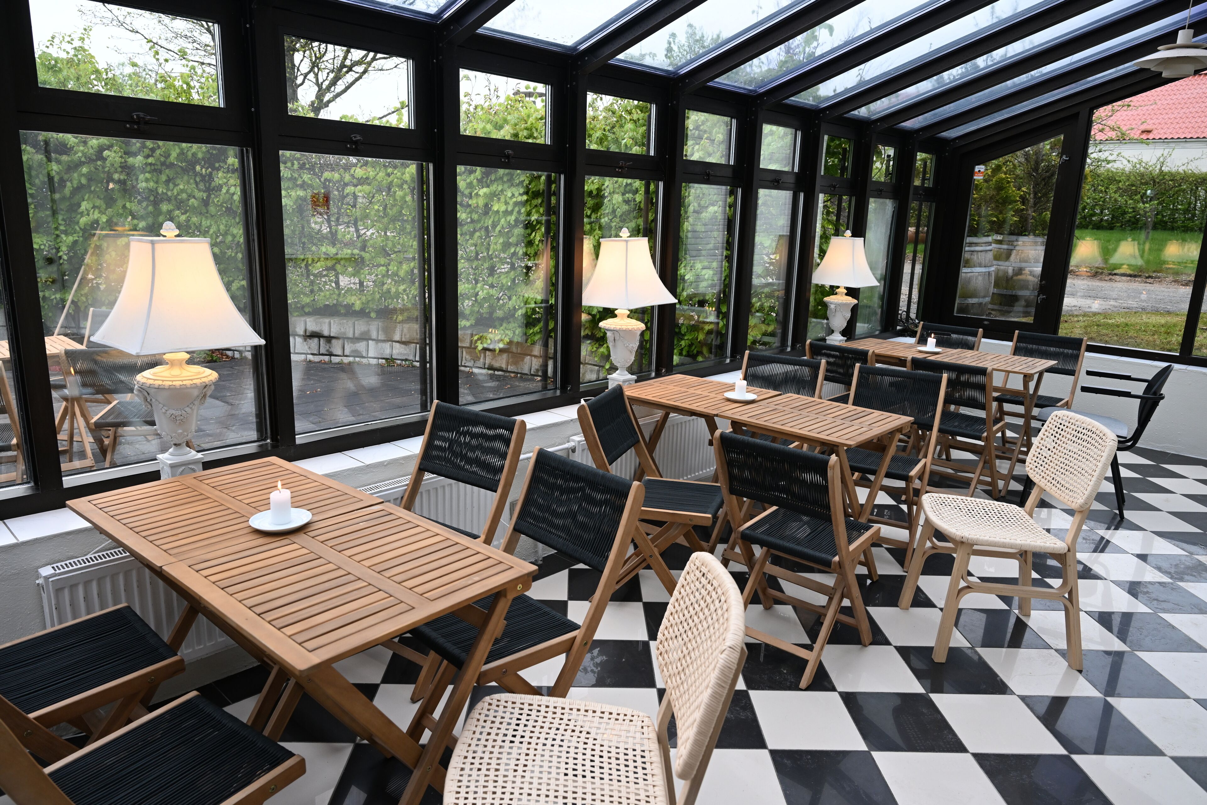 A conservatory with wooden tables and chairs, large windows, and floor lamps.