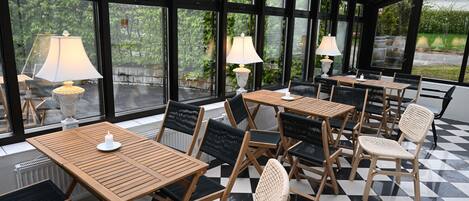 A conservatory with wooden tables and chairs, large windows, and floor lamps.