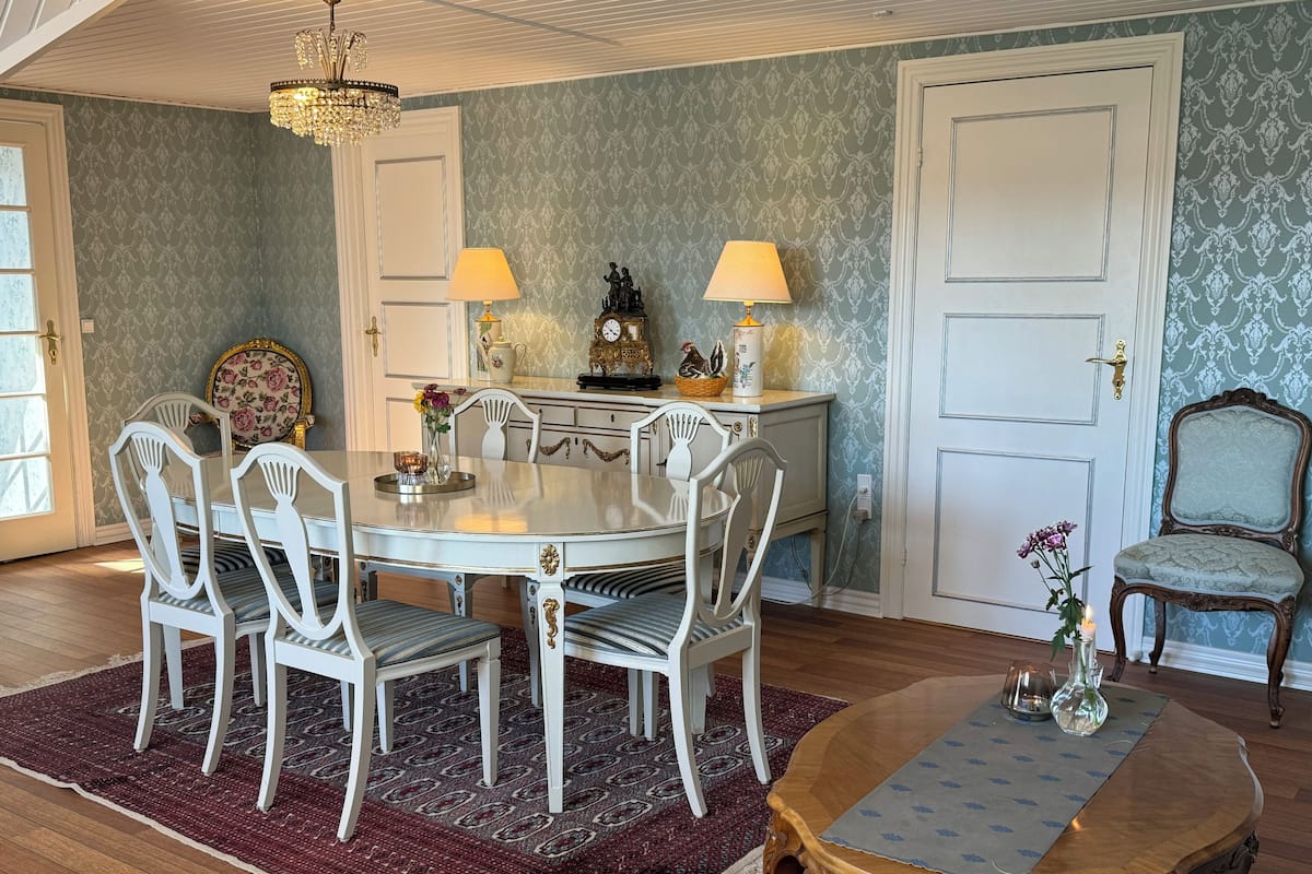 A dining area with a round table, white chairs, a wooden side table, and a patterned rug.