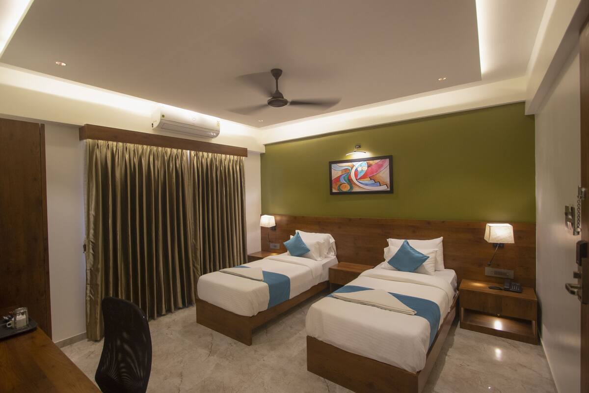 A hotel room with two beds, a ceiling fan, an air conditioning unit, a painting on the wall, and a desk with a chair.