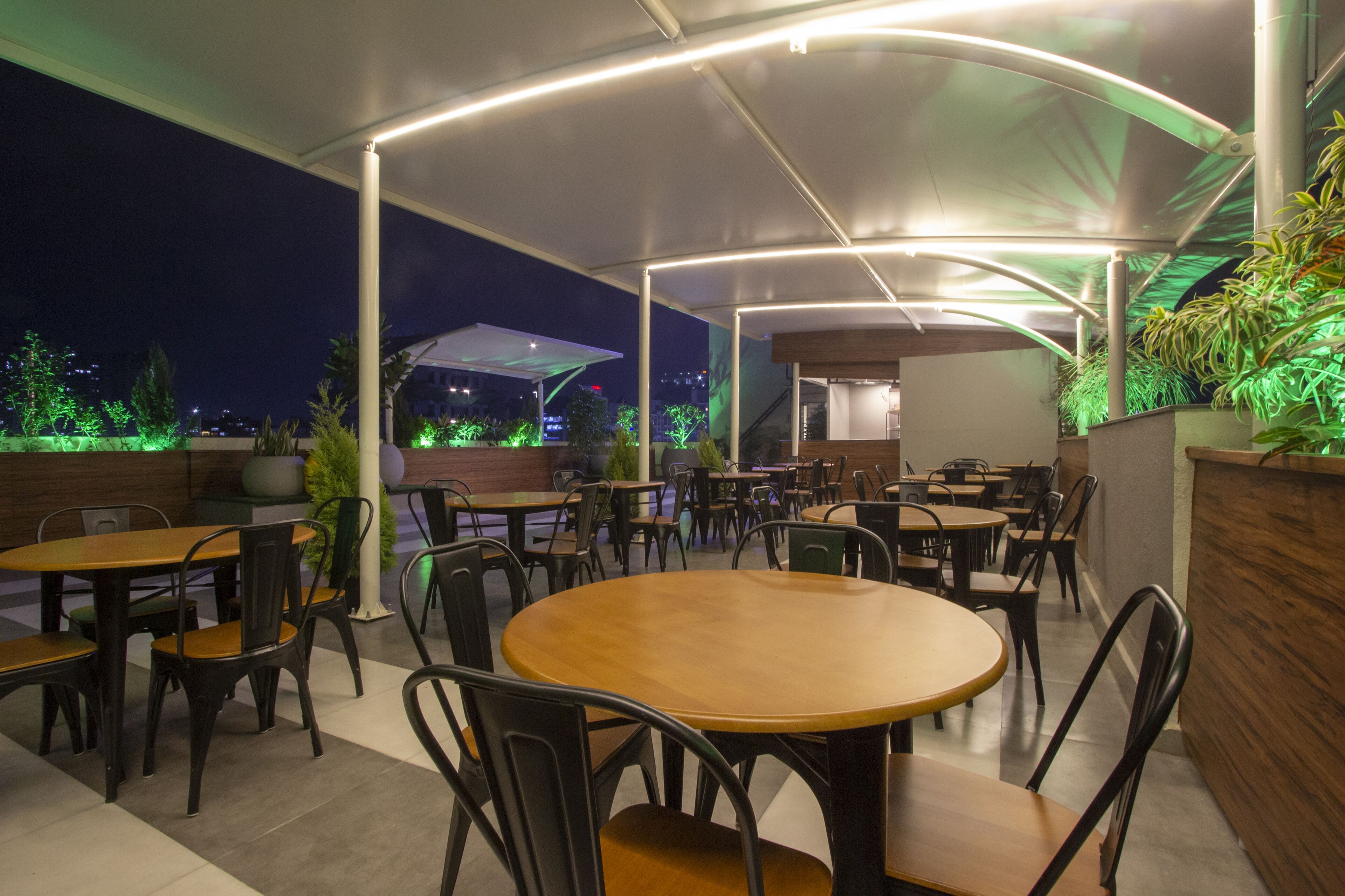 An outdoor cafe area with round tables and chairs, a covered seating area, and potted plants.