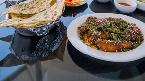 A table with various dishes, including flatbreads, rice, and a fish dish, set outdoors with a view of buildings and greenery in the background. - Monarch Guestline Magarpatta (Pune)