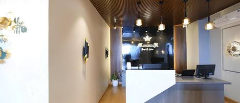 Un mostrador de recepción moderno con techo de madera, iluminación colgante y un área de recepción con pared de vidrio.