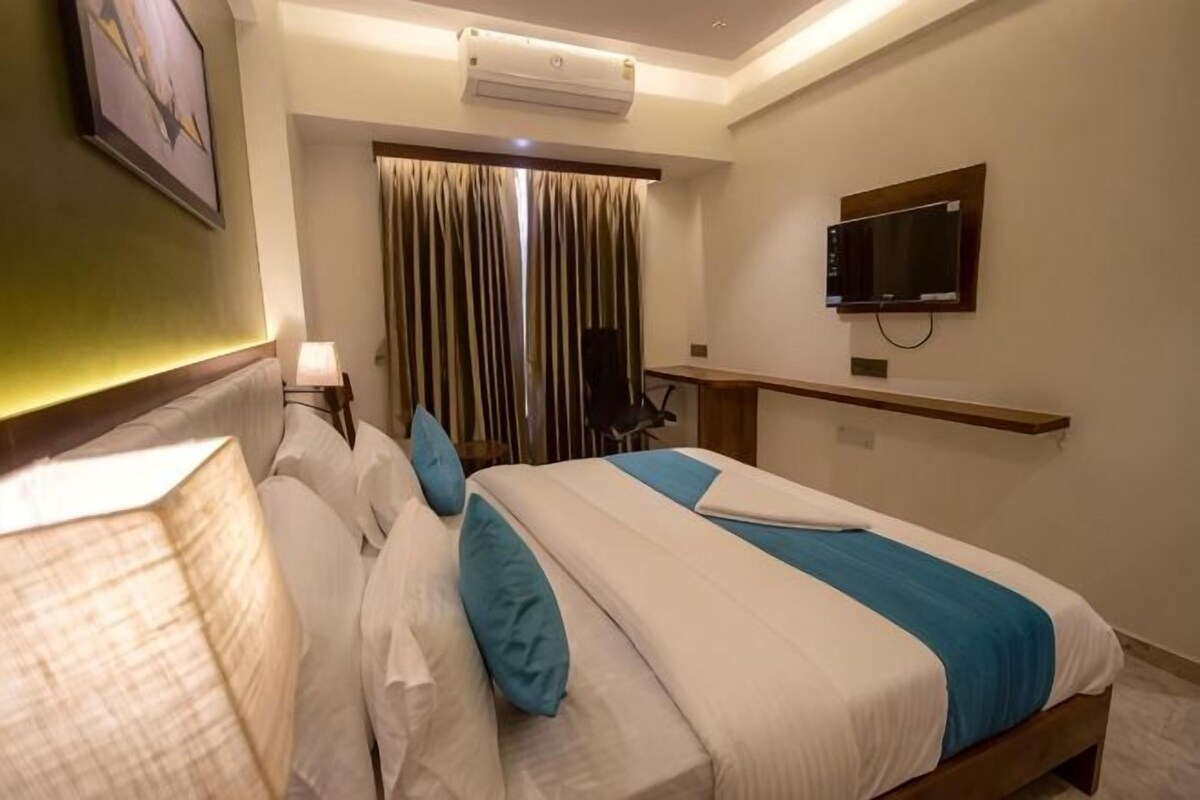 Una habitación de hotel con cama, escritorio, televisión y ventana con cortinas.