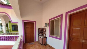 Um corredor com piso de azulejos, porta de madeira, uma janela e uma pequena mesa com cadeiras.