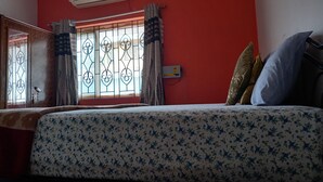 Quarto com cama, janela com grades de ferro decorativas, ar condicionado e parede vermelha.