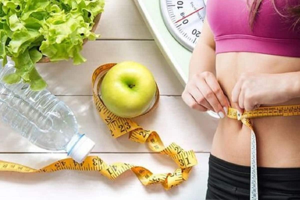 A scale, a measuring tape, a bottle, and an apple on a table.