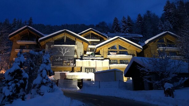 Eine Lodge mit mehreren Holzhütten, einem Schild mit der Aufschrift 'L'APPartement' und einer verschneiten Landschaft.