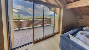 Ein Zimmer mit einer großen Glasschiebetür, die auf einen Balkon mit Holzboden und Bergblick führt.