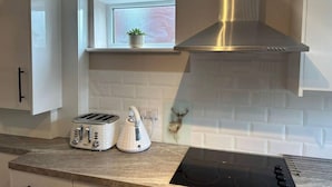 A modern kitchen with white cabinets, a built-in oven, a stainless steel range hood, a toaster, and a kettle on the countertop. - Immaculate 1-bed House in Newtown, Disley (Stockport)