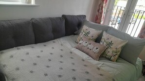 A bedroom with a grey sofa, a bed with a patterned bedspread, and floral pillows. - Immaculate 1-bed House in Newtown, Disley (Stockport)