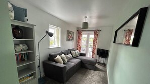 A living room with a grey sofa, a bookshelf, a floor lamp, and a TV. - Immaculate 1-bed House in Newtown, Disley (Stockport)