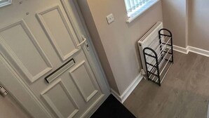 A hallway with a white door, a window with blinds, a radiator, and a black metal rack. - Immaculate 1-bed House in Newtown, Disley (Stockport)