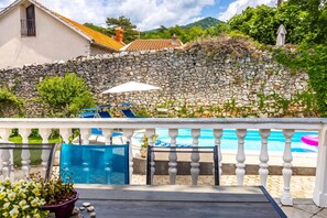 A poolside area with stone walls, a white fence, and blue lounge chairs. - Meja Stone House With Pool (Bakar)