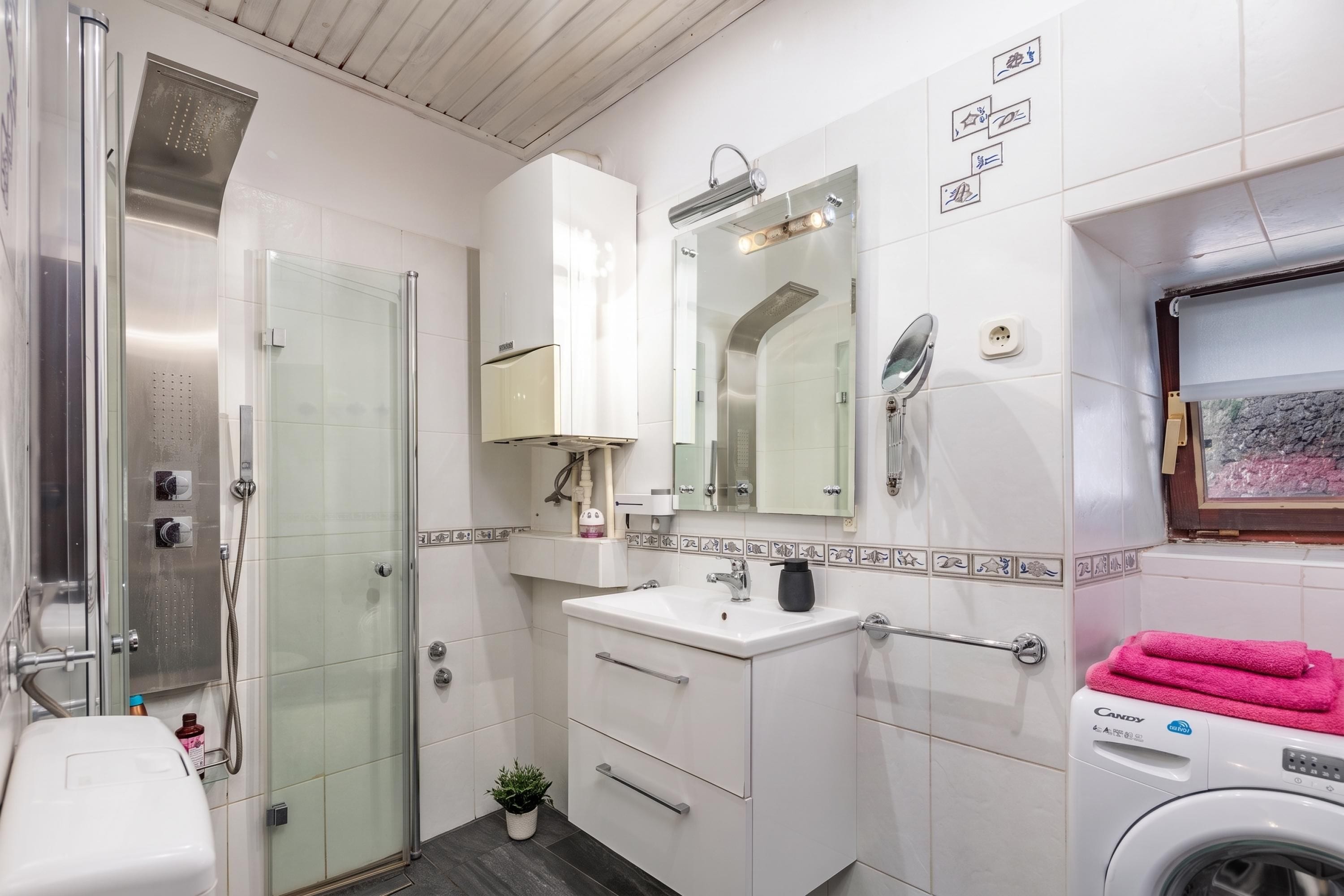 A modern bathroom with a glass-enclosed shower, a white sink with a mirror, and a washing machine.
