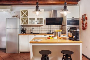 A modern kitchen with white cabinetry, a central island with stools, a built-in oven, and a microwave. - Meja Stone House With Pool (Bakar)