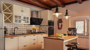 Una cucina con mobili bianchi, un piano di lavoro in legno, un piano cottura integrato, un lavello, utensili appesi e una macchina da caffè.