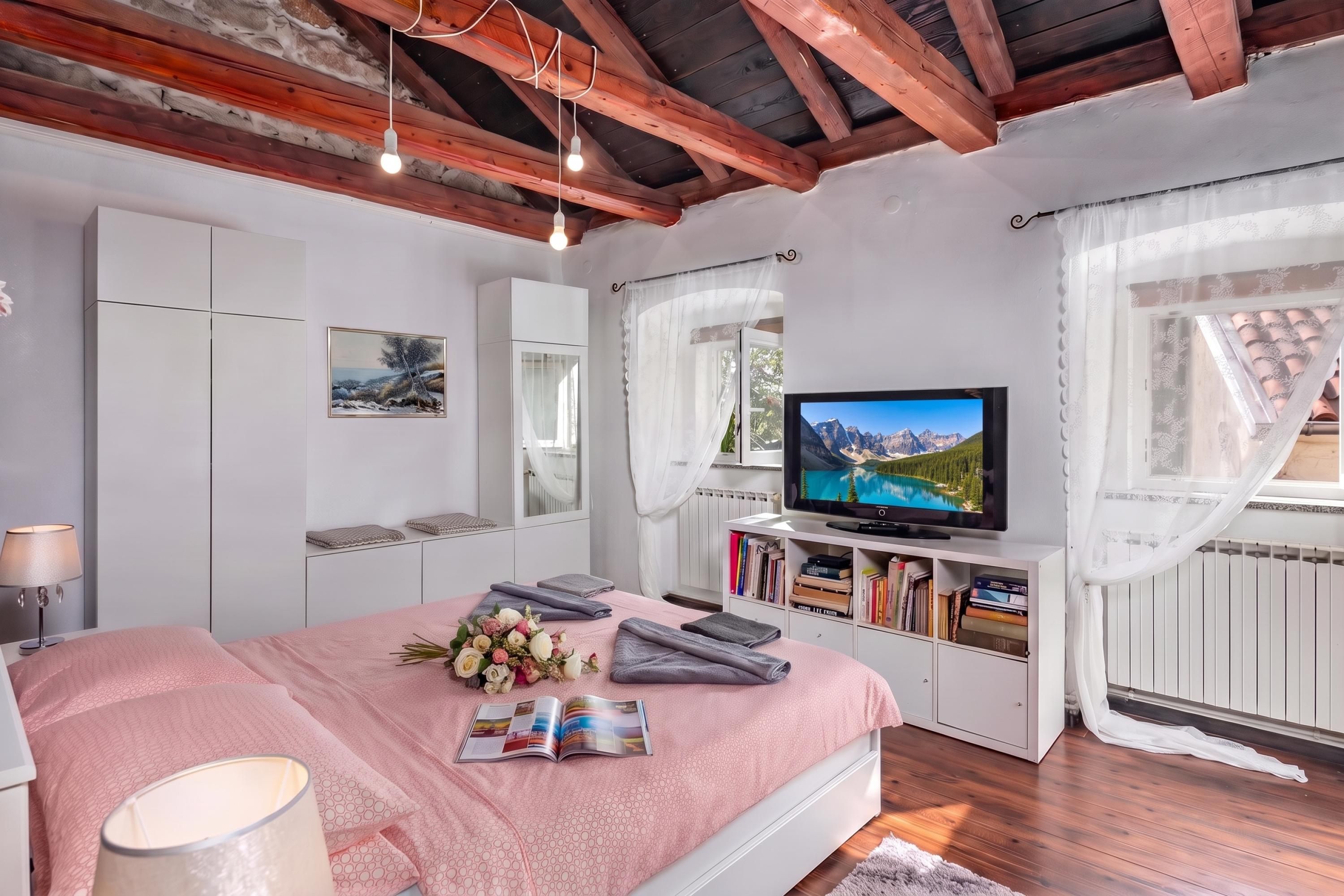A bedroom with a bed, a television, a bookshelf, and a window with curtains.