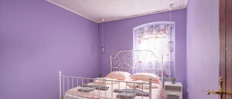 Un dormitorio con una cama individual, una mesita de noche, una pequeña mesa, una ventana con cortina y suelo de madera.