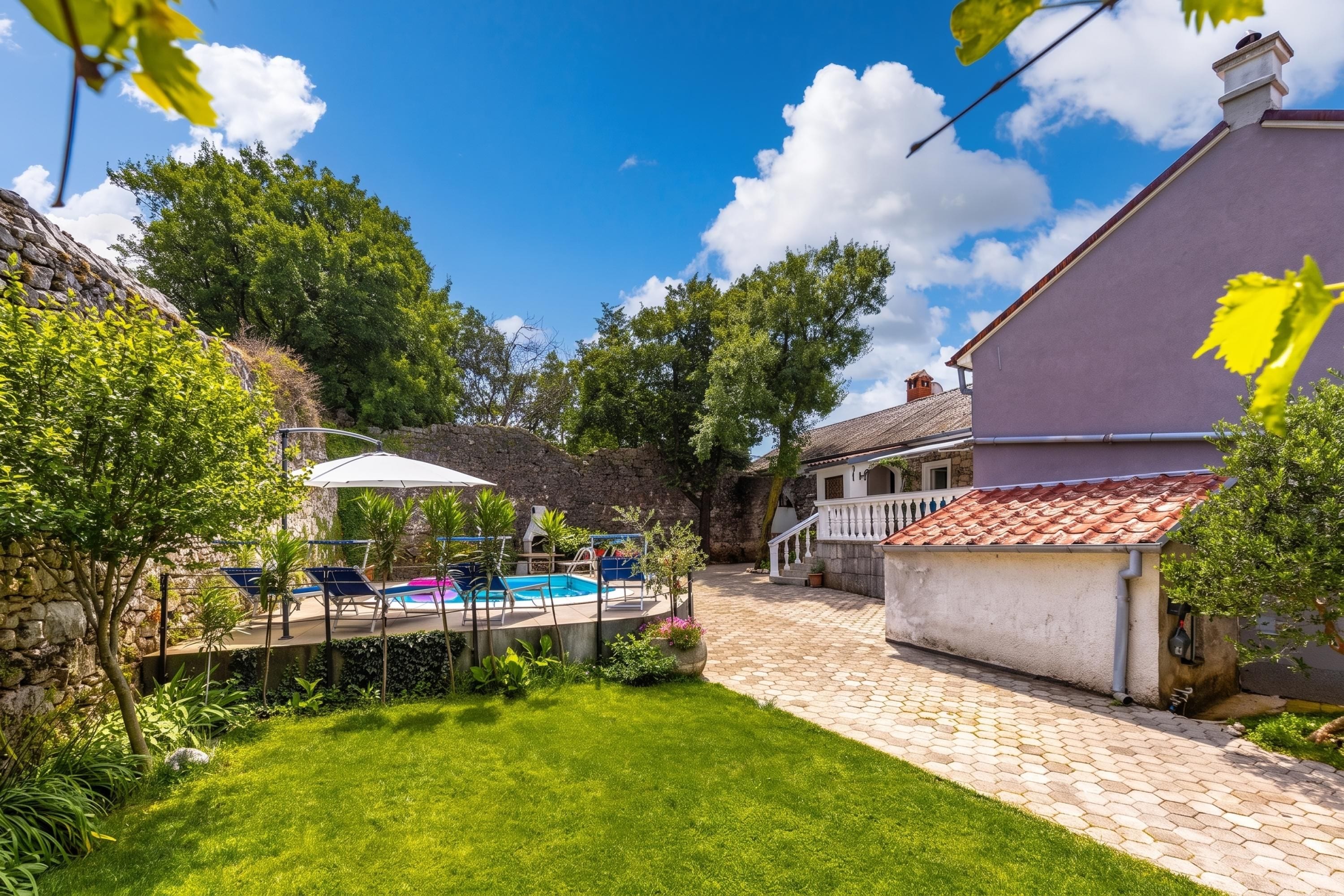 Ein Garten mit Swimmingpool, Liegestühlen und einem gepflasterten Weg, der zu einem Gebäude führt.