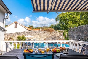 A terrace with a dining table set for breakfast, overlooking a pool and a stone wall. - Meja Stone House With Pool (Bakar)